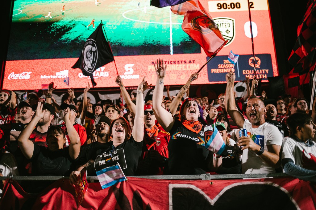 Rising fans throw their hands up in the air in celebration following a Rising goal